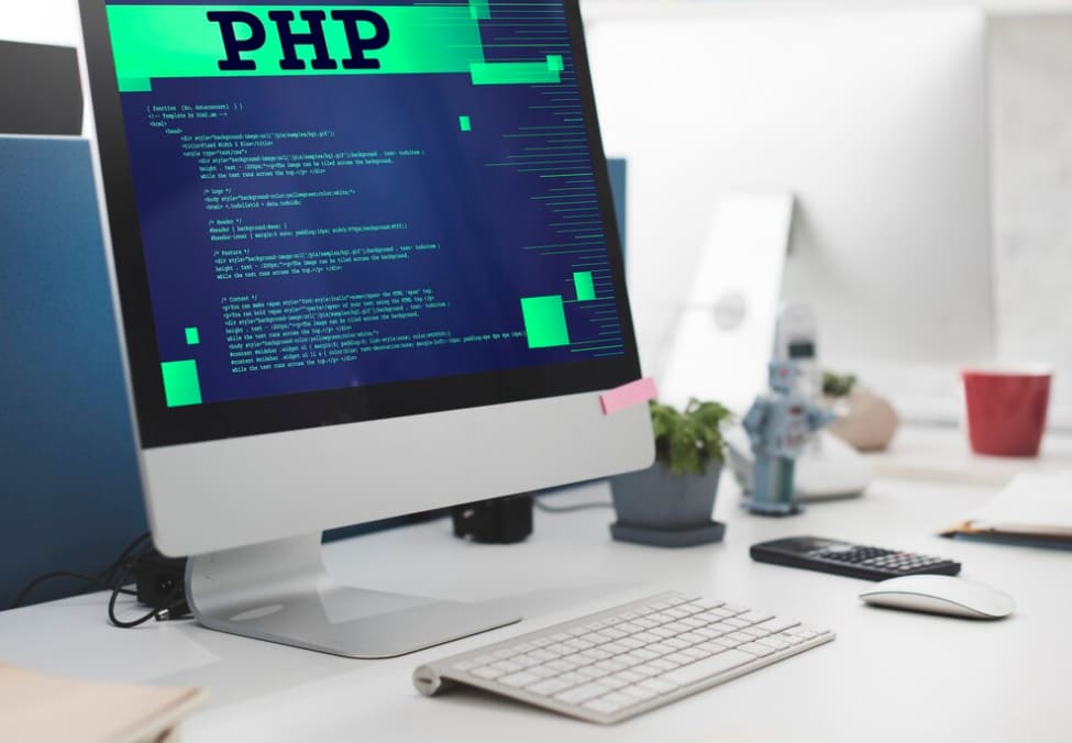 a computer screen with php word on it and keyboard on white table with flower and red cup on it